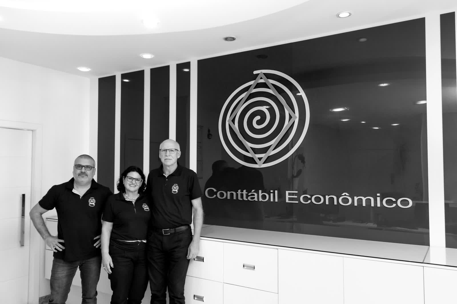 Equipe do Escritório Conttábil Econômico na recepção, em frente ao símbolo da marca na parede